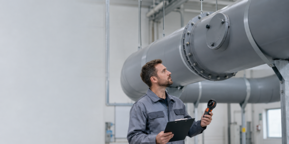 Maintenance engineer inspecting a flanged PP ventilation duct run with an anemometer and checklist
